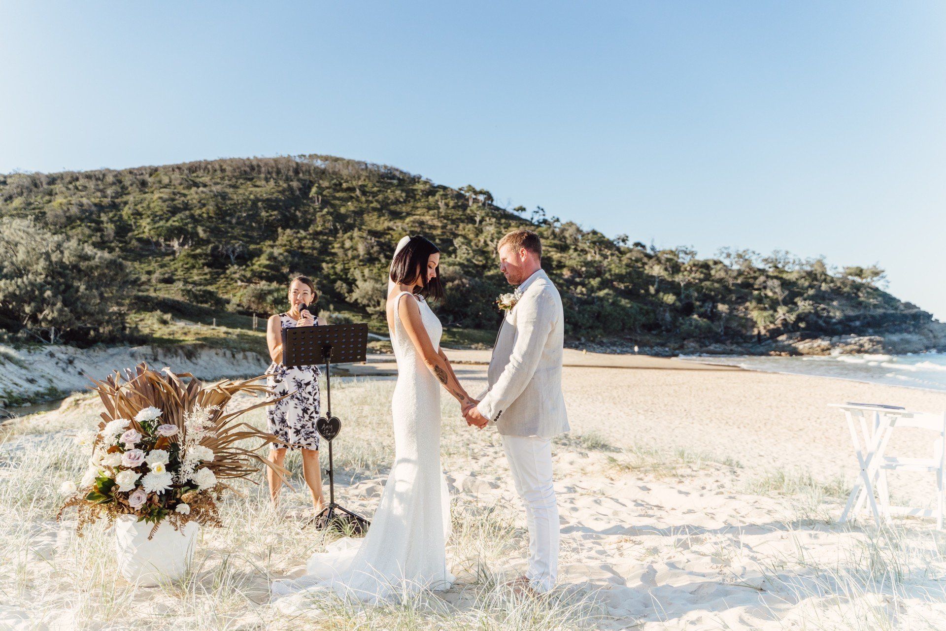 couple on a grassy hill eloping at sunshine beach with ocean and floral display in pot, noosa headland behind them