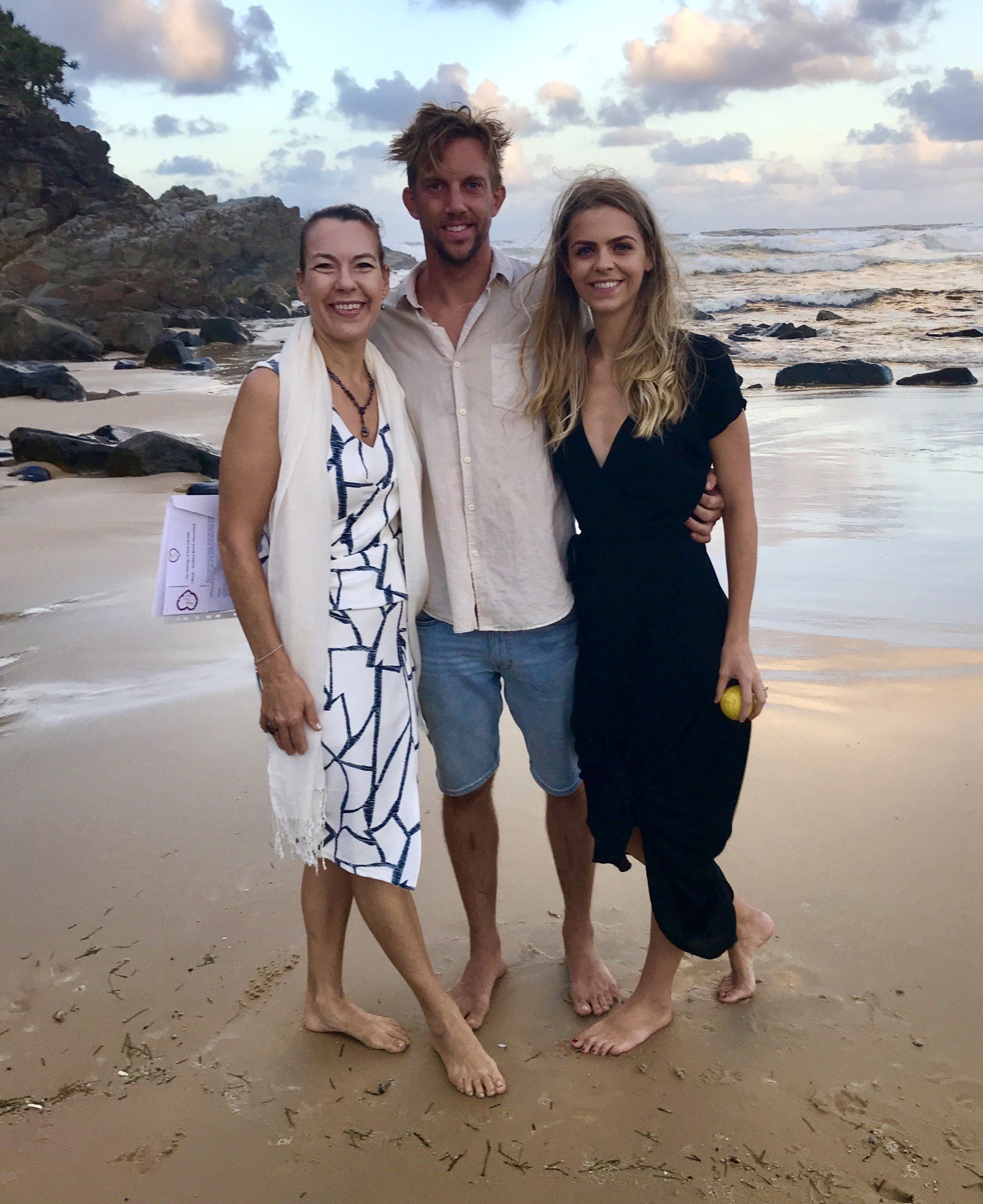bridal couple and celebrant all bare feet in sand, just eloped at sunshine Beach, Noosa, bride wearing black dress, groom in beige