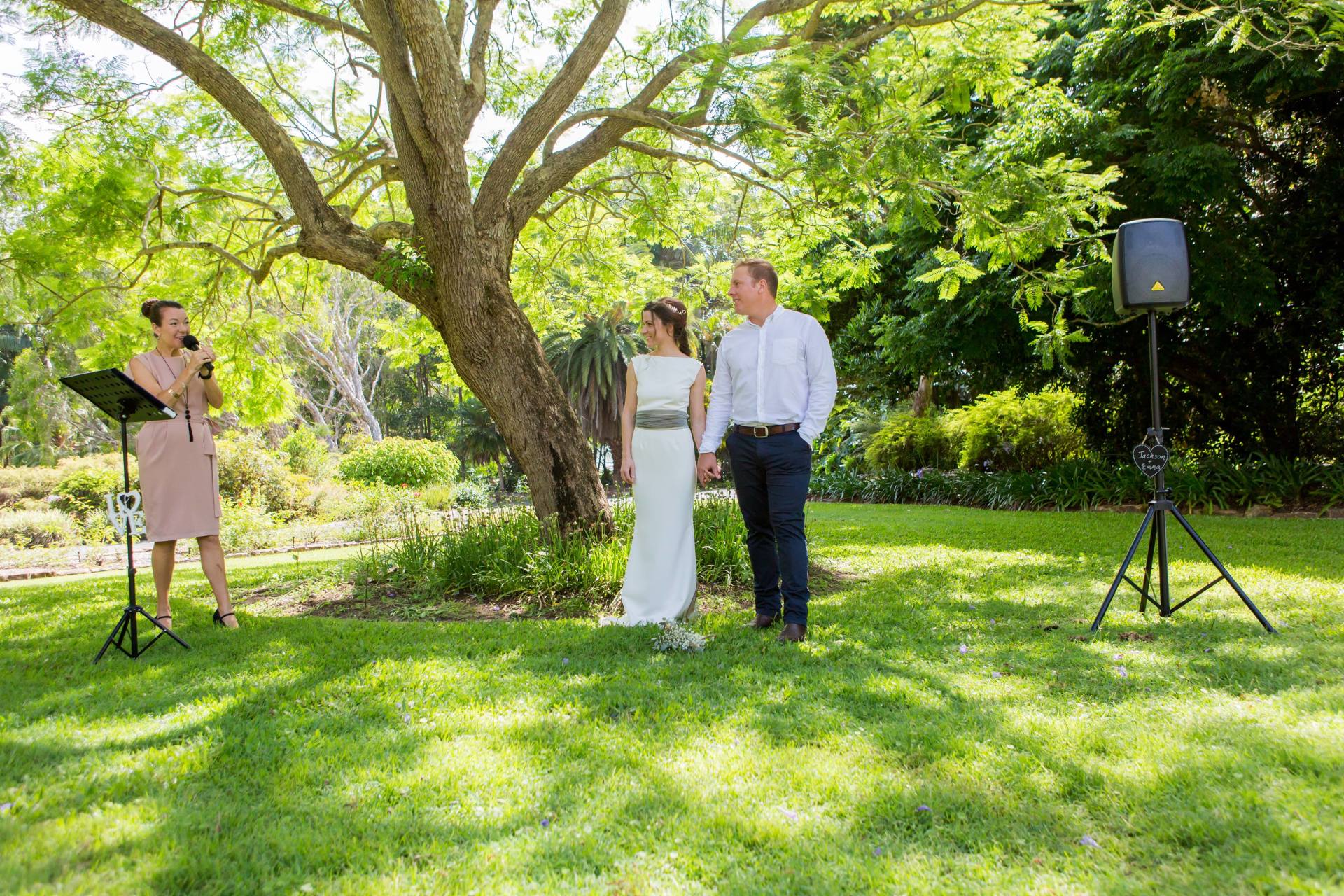 couple marry under jacaranda tree in Noosa botanical gardens, celebrant officiating the ceremony with smiles