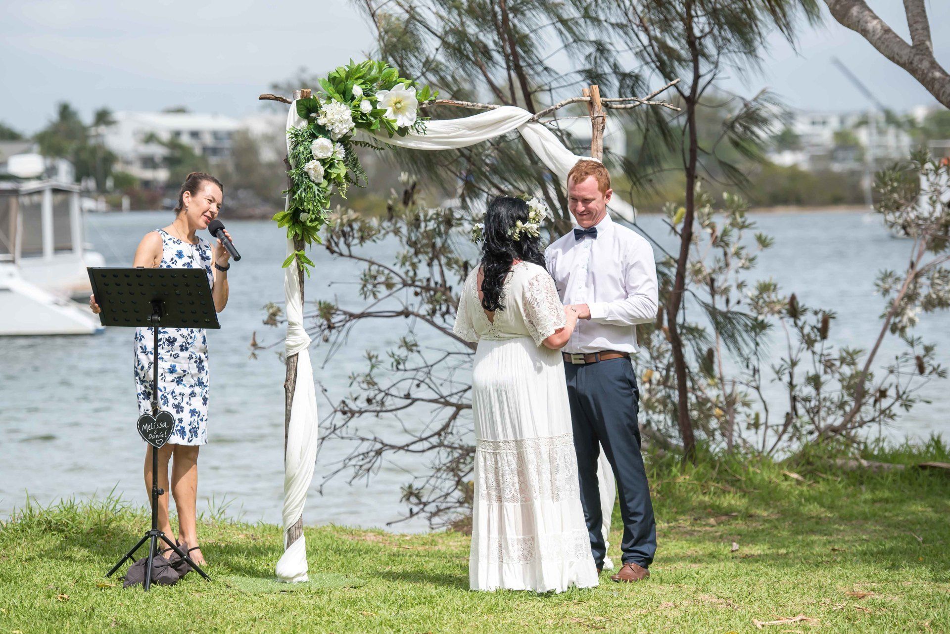 smiling Noosa celebrant marrying couple by the Noosa river, boats in background on the water