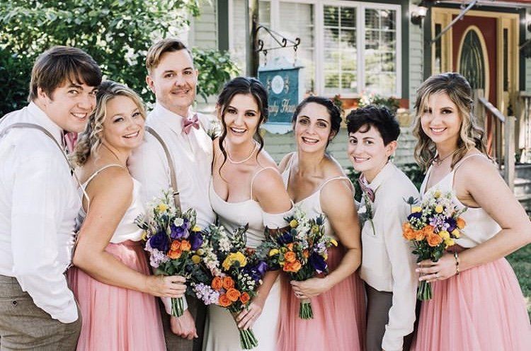 mixed bridal party of girls and guys all smiling wearing brown and pink with bright flowers and big smiles at sunny coast wedding