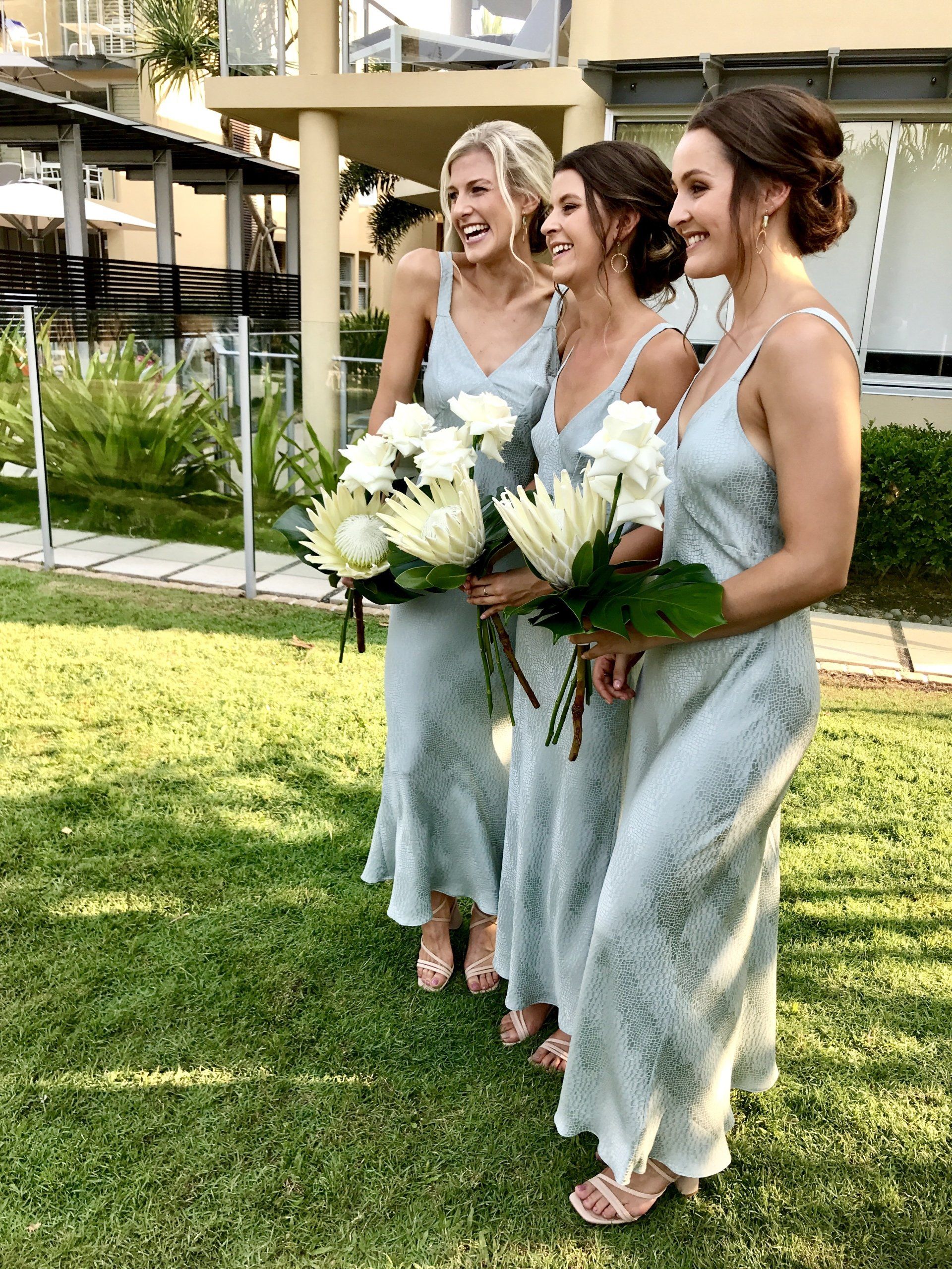 three very stunning bridesmaids in mint green holding big white bouquets with hair styled and laughing at a Noosa wedding