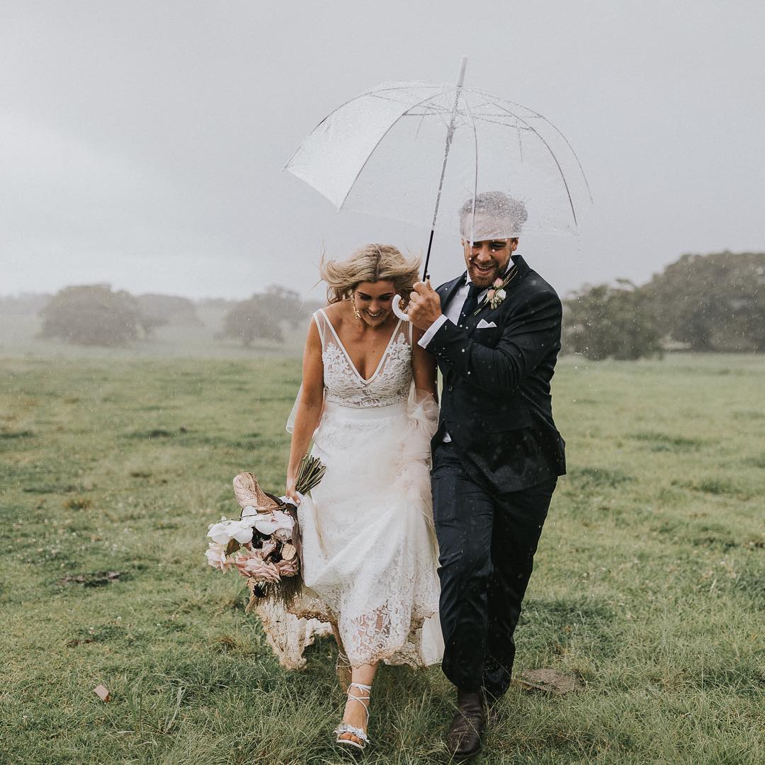 bridal couple run in rain under umbrella at hinterland rainy day wedding