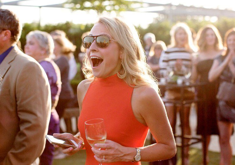 guest wearing orange and sunglasses and earrings with open mouth full of surprise at surprise wedding
