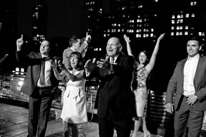 smartly dressed guests clapping and cheering at nighttime rooftop surprise wedding