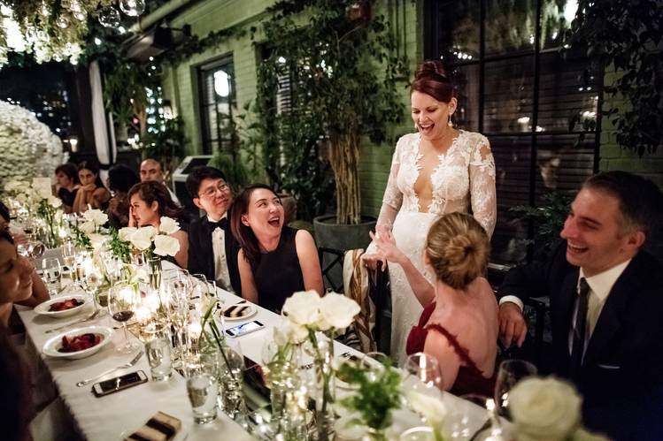 smart guests all chatter and cheer for pretty bride in white dress with v neck at long table with glasses and white flowewrs and candles