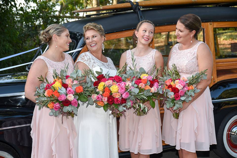 bride with 3 bridesmaids in pink with huge bouquets waiting by Woody station wagon car before her Noosa wedding