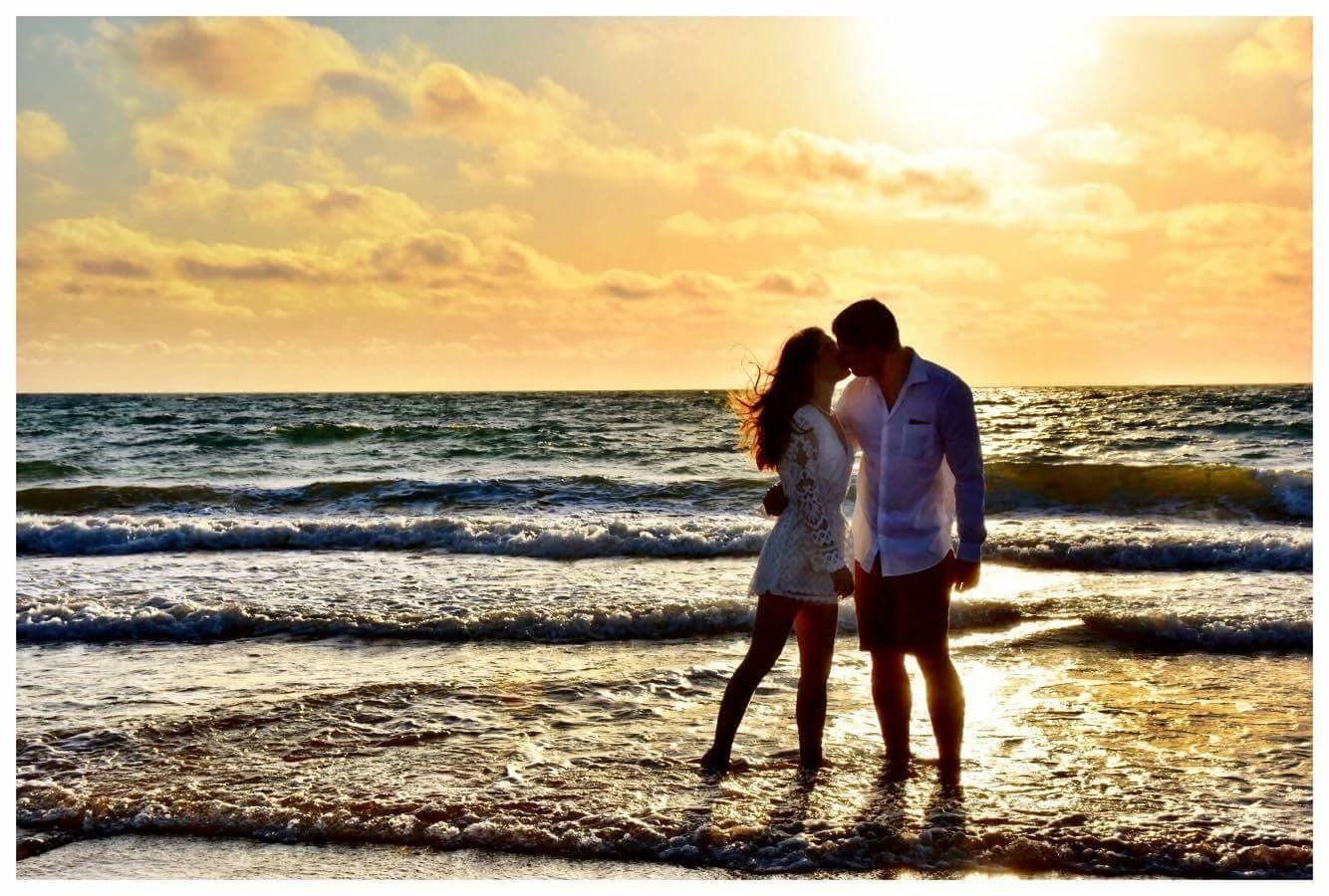 couple just eloped kiss in ocean at sunrise with yellow sky behind them