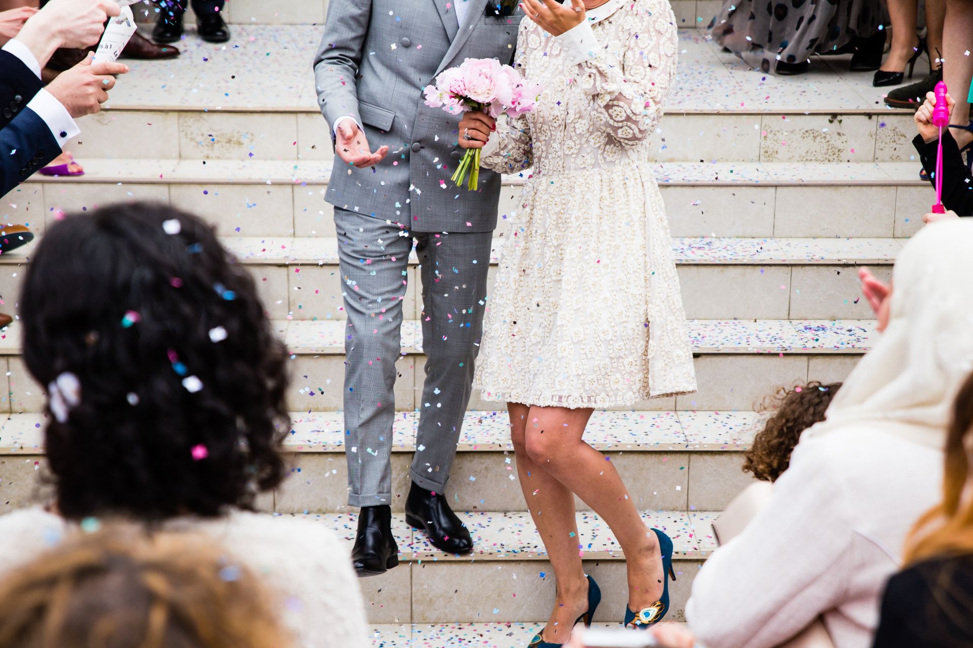 couple on building steps after having registry wedding, bride in white dress with pink posy, groom in grey suit
