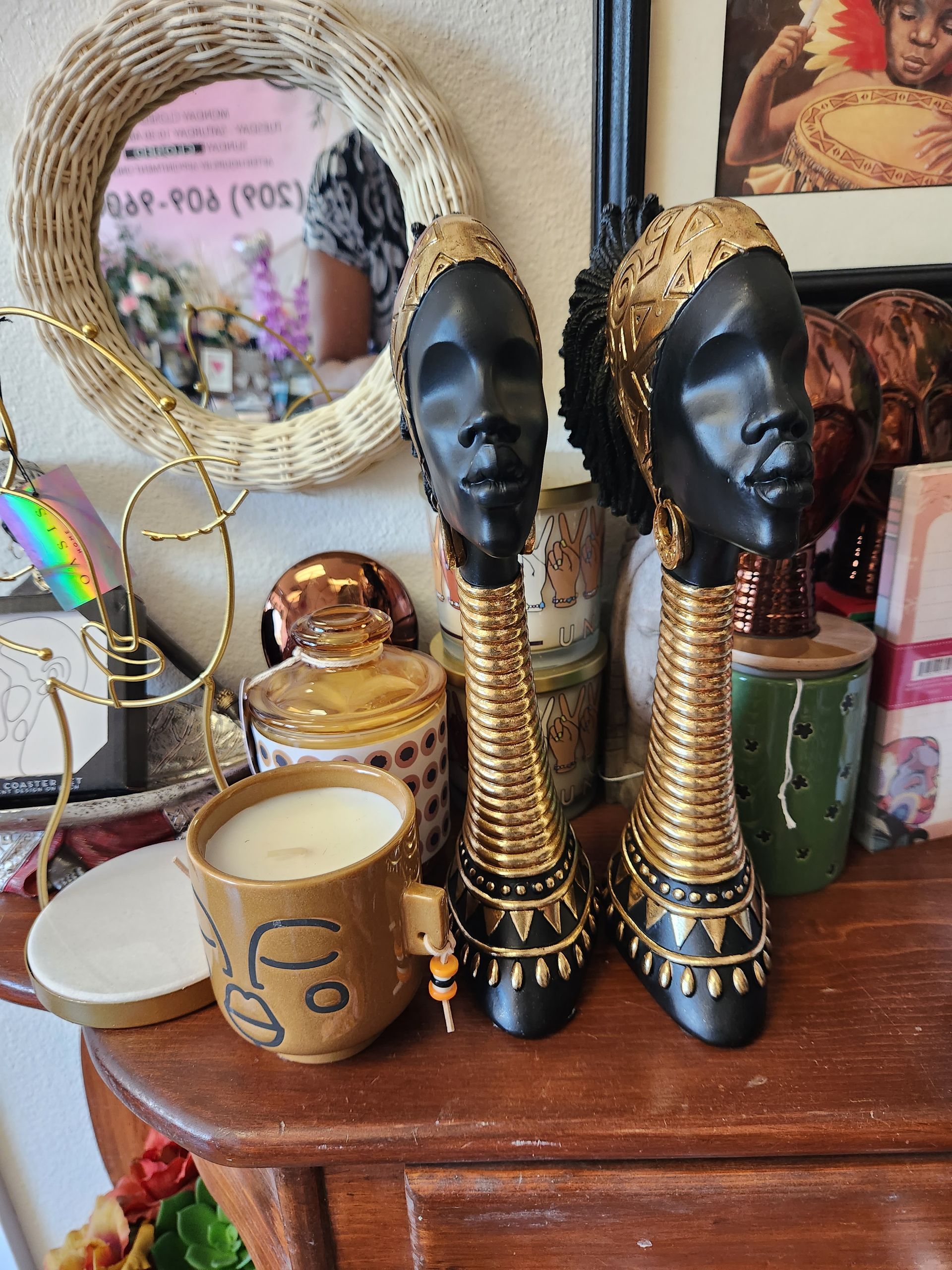 Two statues of african women are sitting on a wooden table next to a candle.