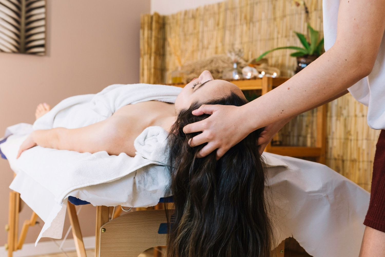 Person receiving a head massage on a massage table indoors; hands of masseuse in frame.