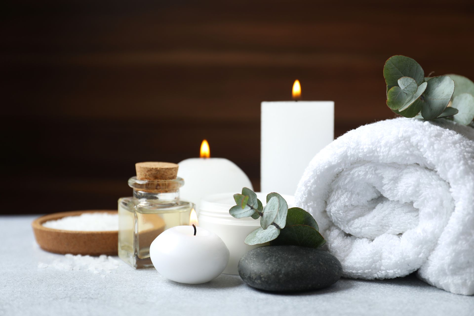 Spa scene with candles, rolled towel, greenery, oils, and a salt bowl.