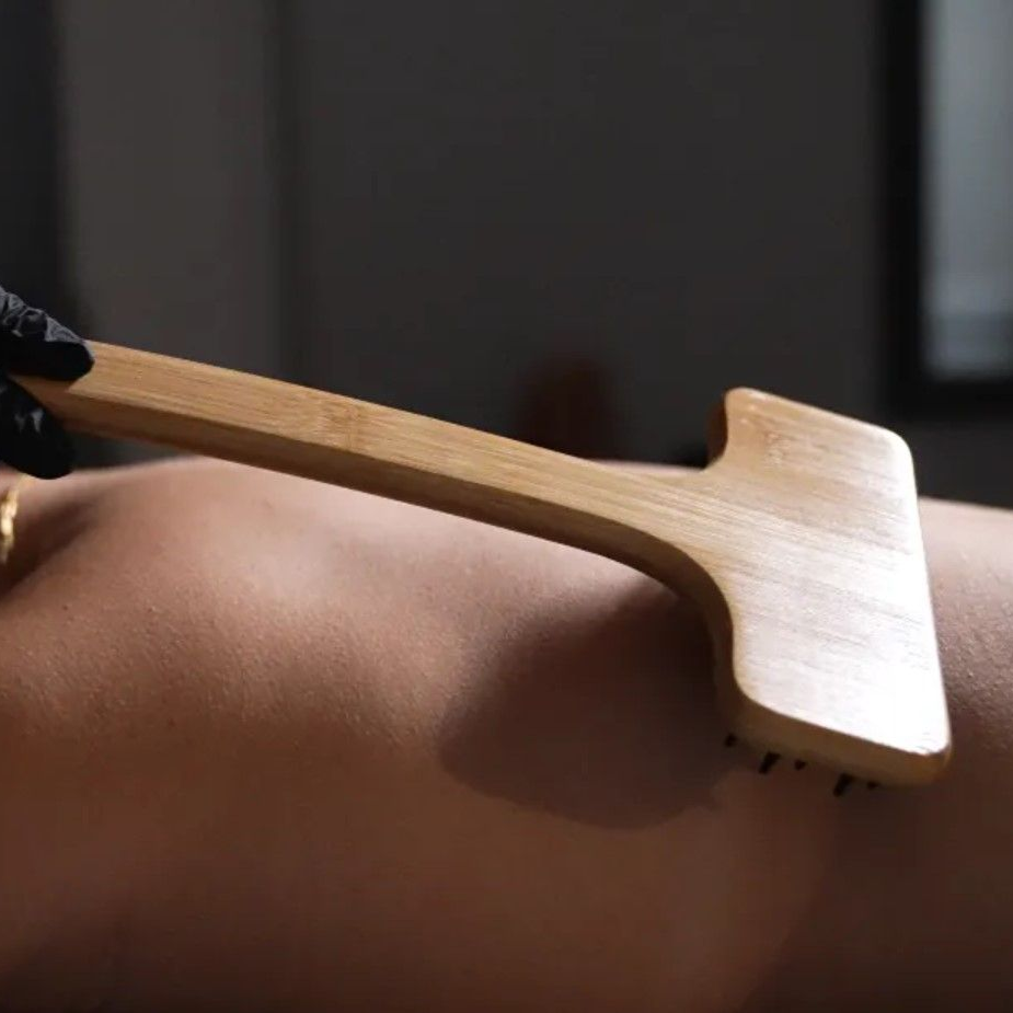 Person receiving back massage with wooden tool. Black gloved hand.