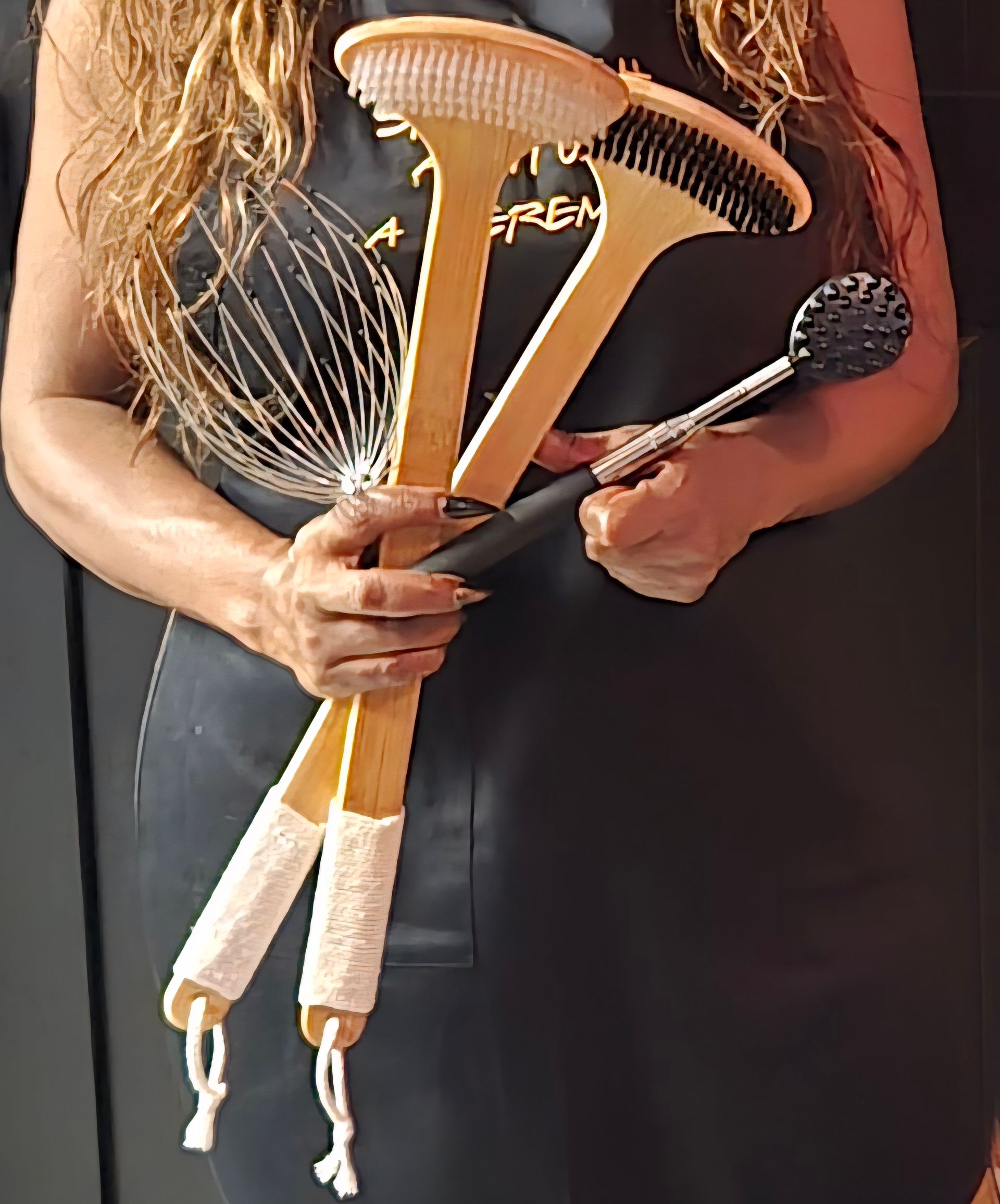 Woman holding spa brushes, black apron, light skin, long blonde hair.