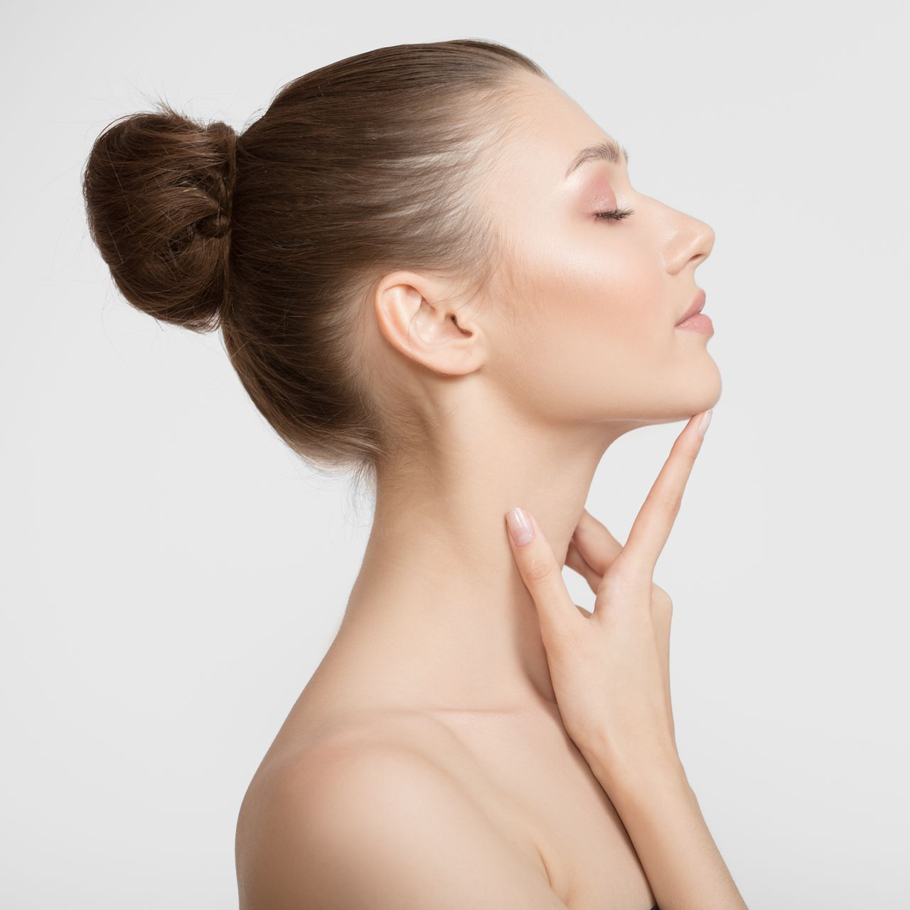 Woman with a hair bun, touching her chin, side view.