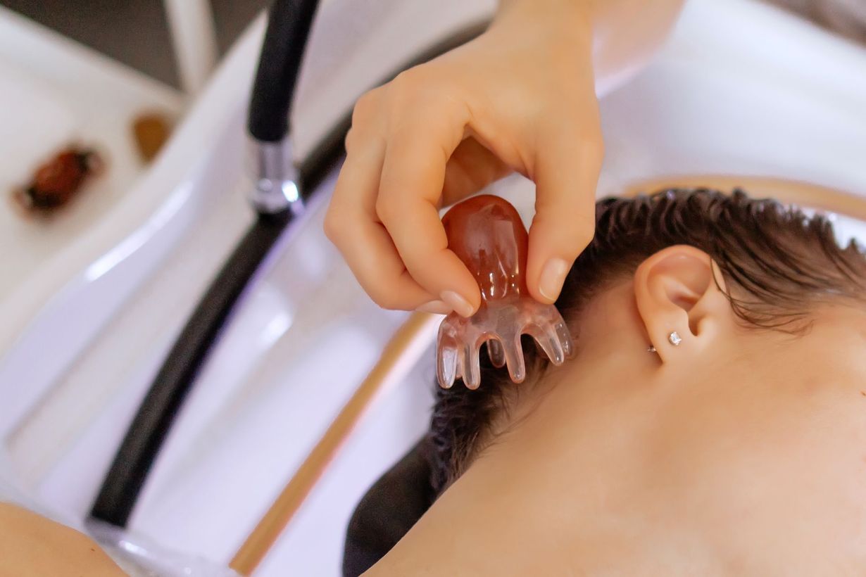 Hand massaging a person's neck with a clear, octopus-shaped tool in a salon setting.