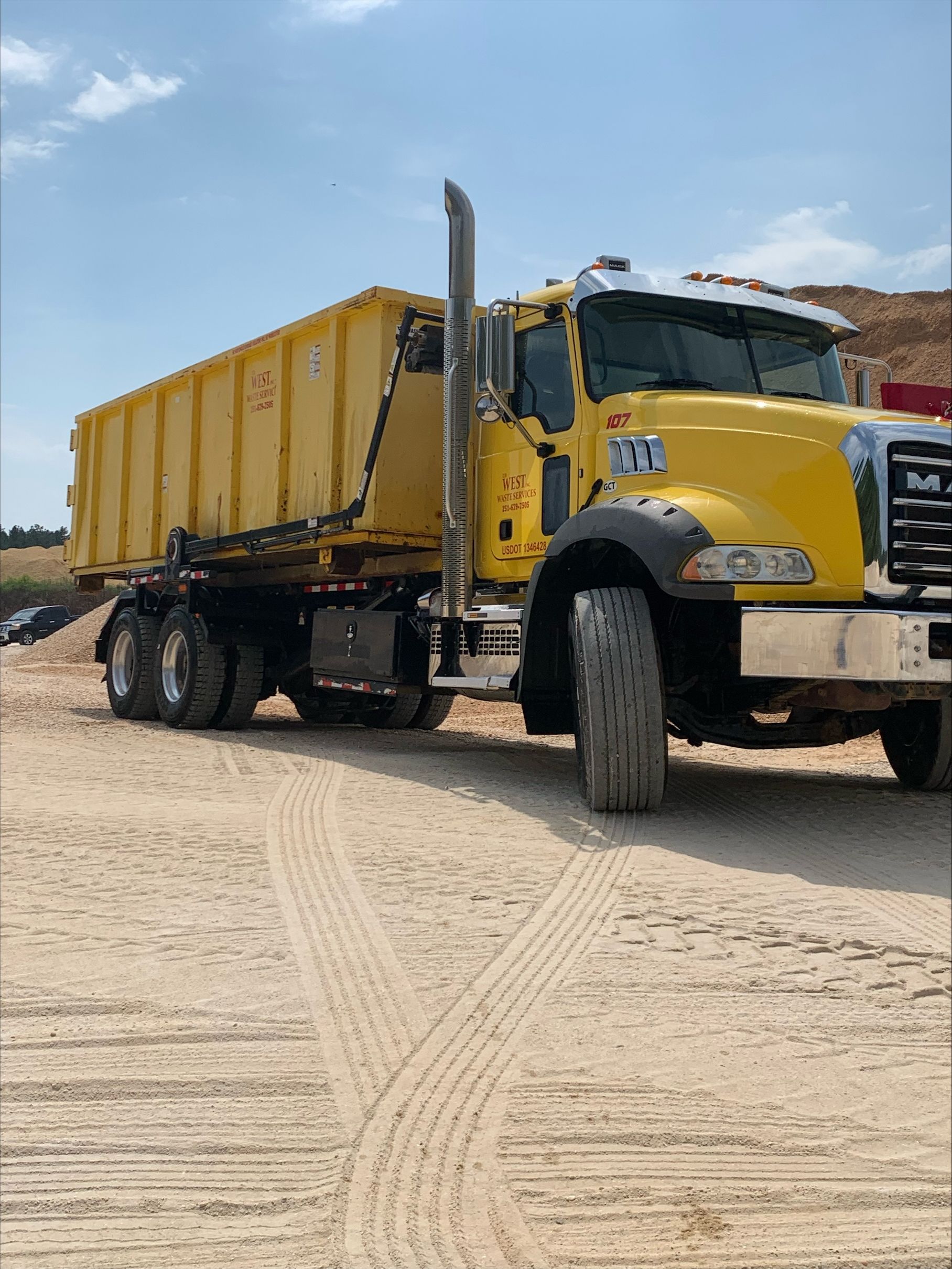 Yellow dump truck on dirt, with a blue sky in the background.