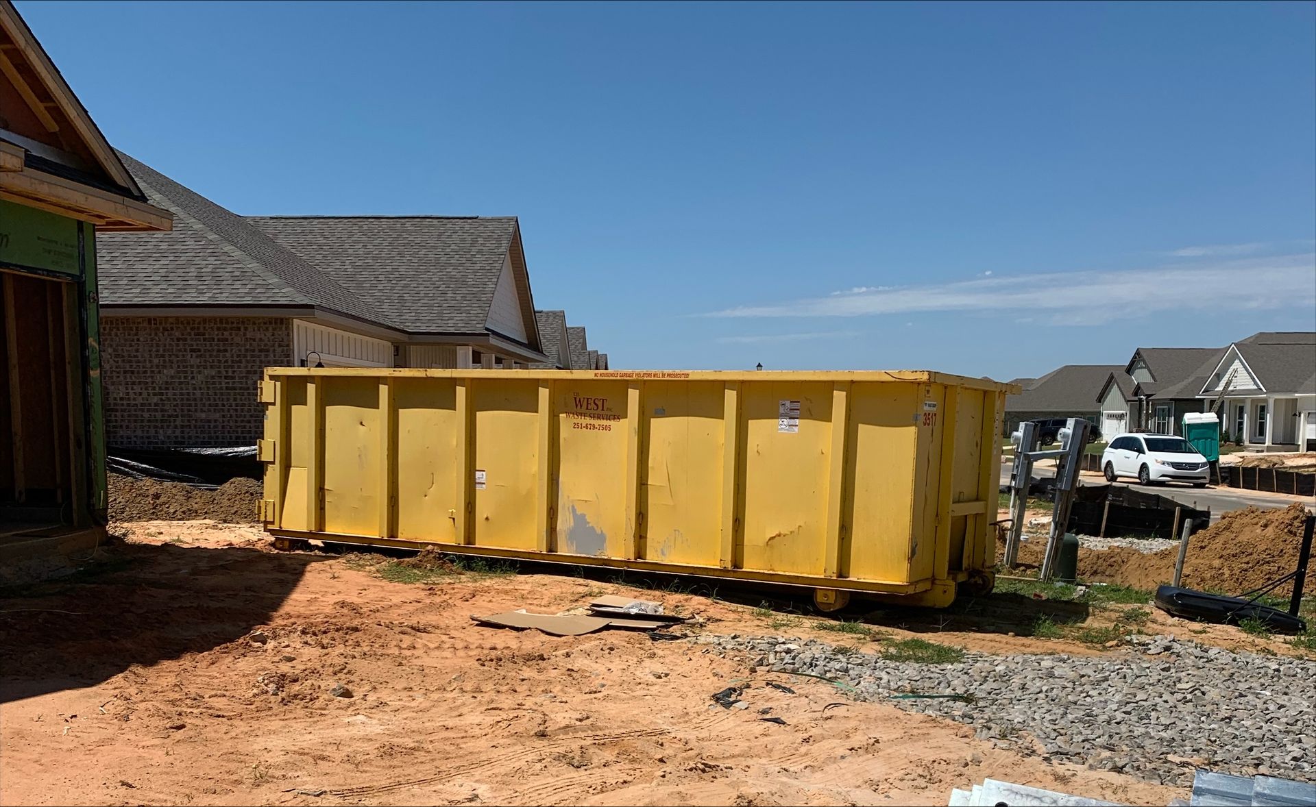 Metal dumpster filled with various household debris, in a residential driveway.