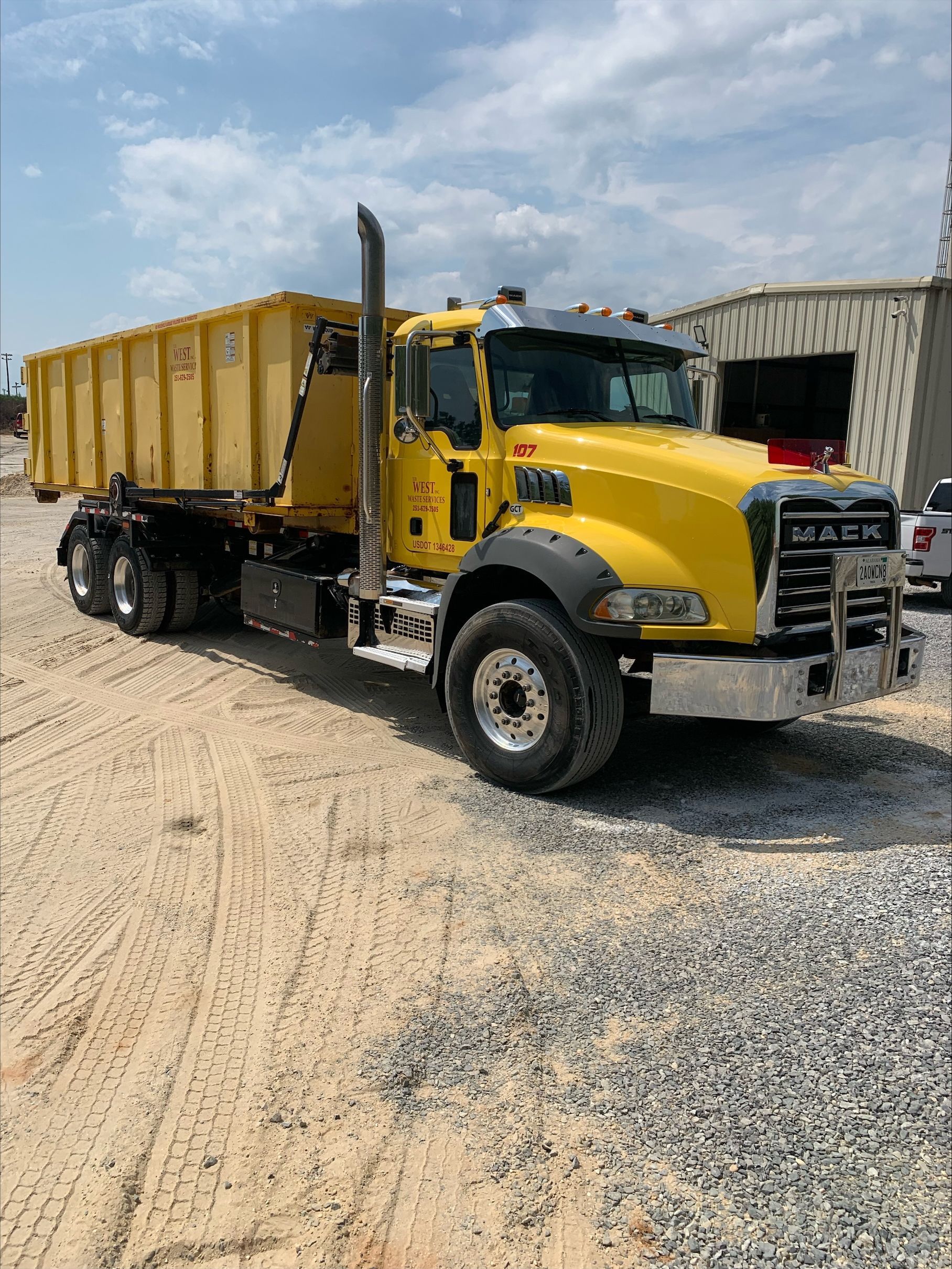 Yellow Mack dump truck on gravel under a cloudy sky.