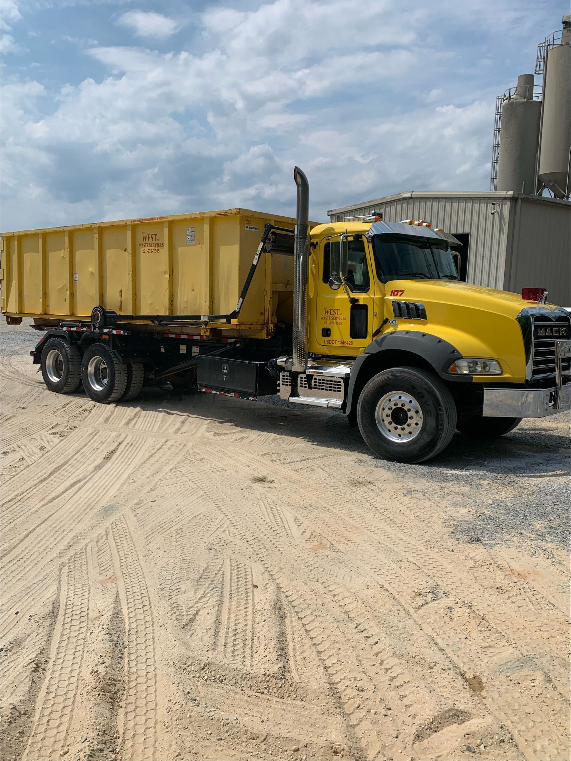 Yellow dump truck parked on gravel, industrial setting.