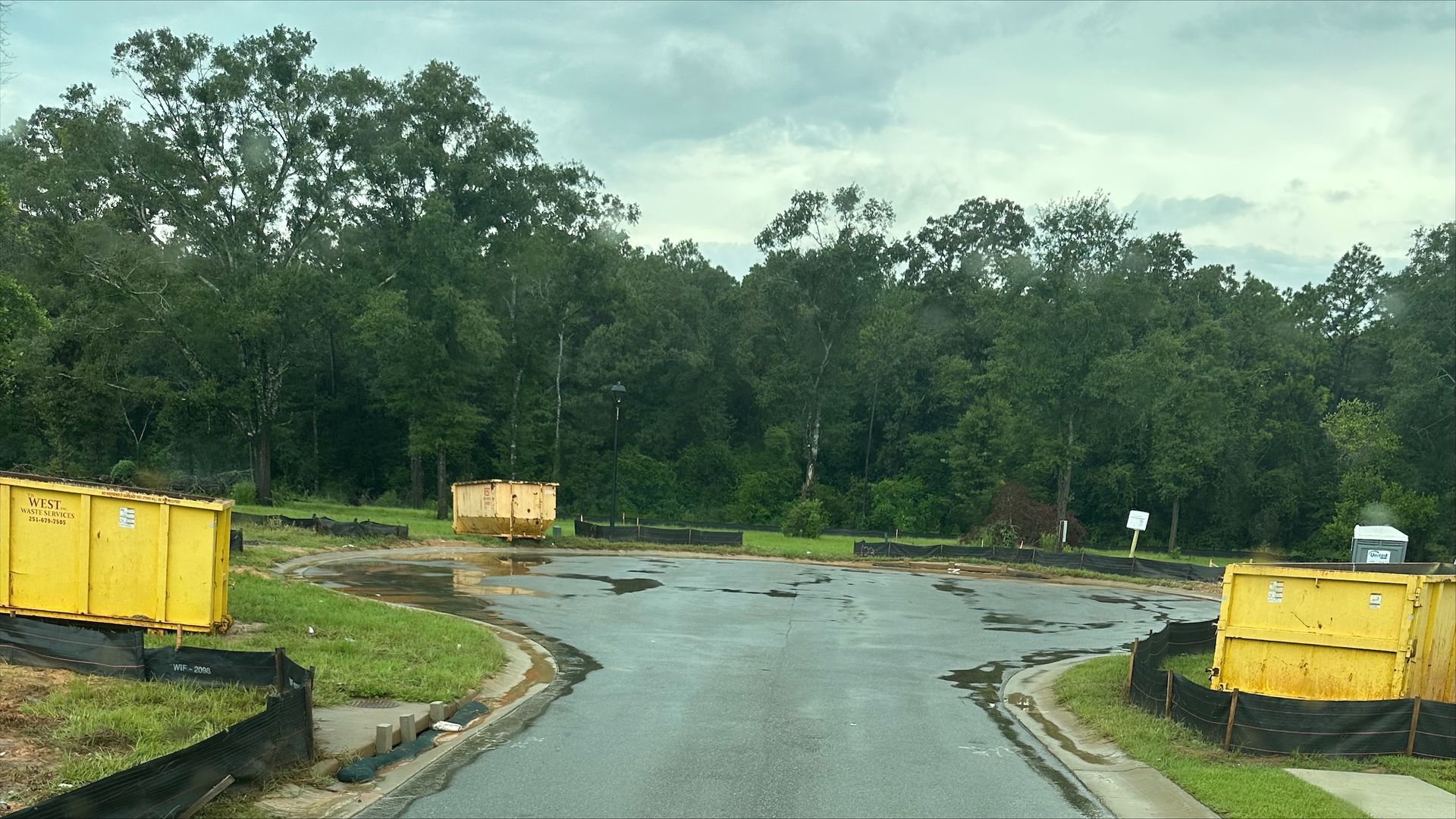 Construction site with a portable toilet and a large dumpster. Buildings in the background.