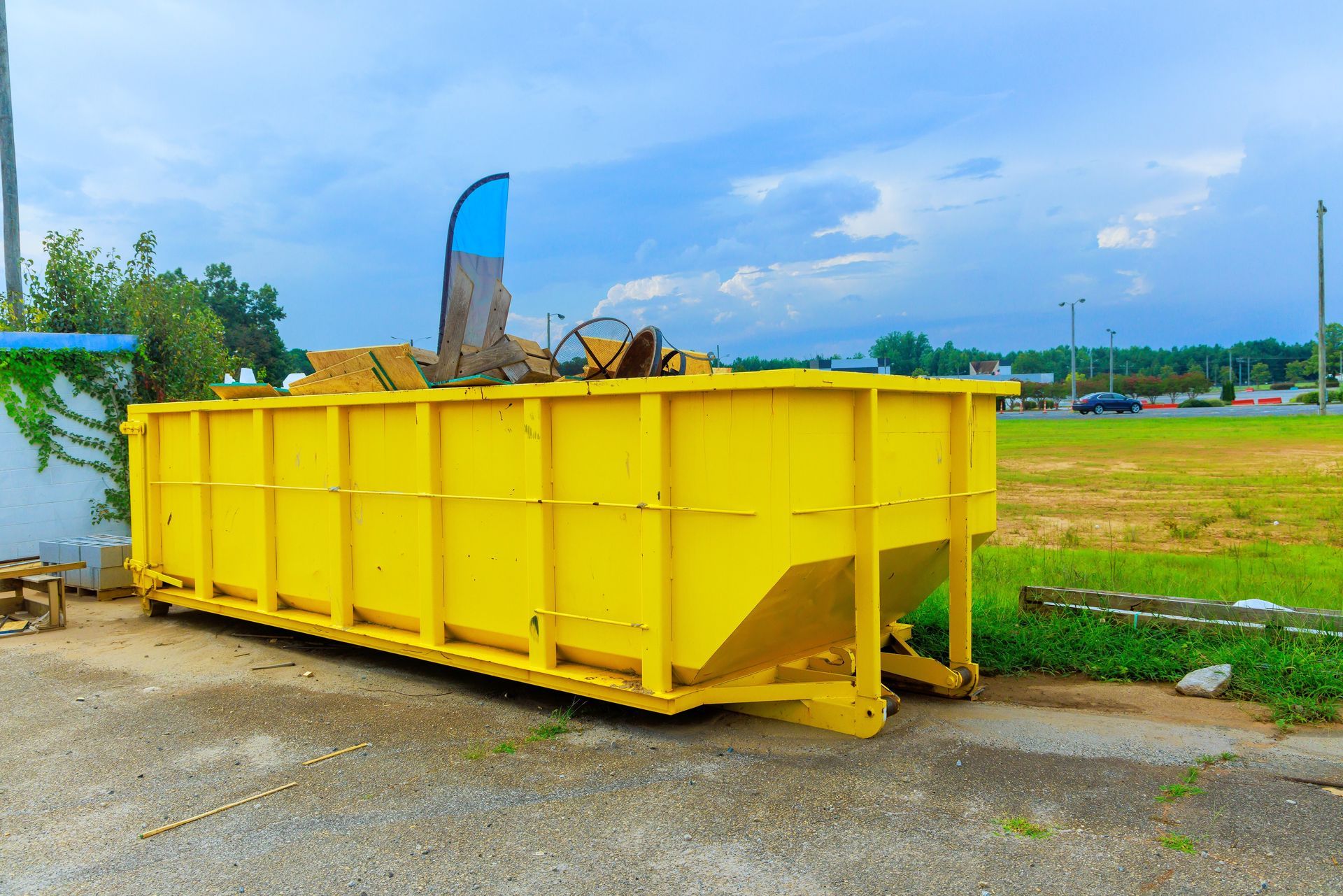 Yellow dumpster filled with debris on pavement, with a blue and black sign on top.