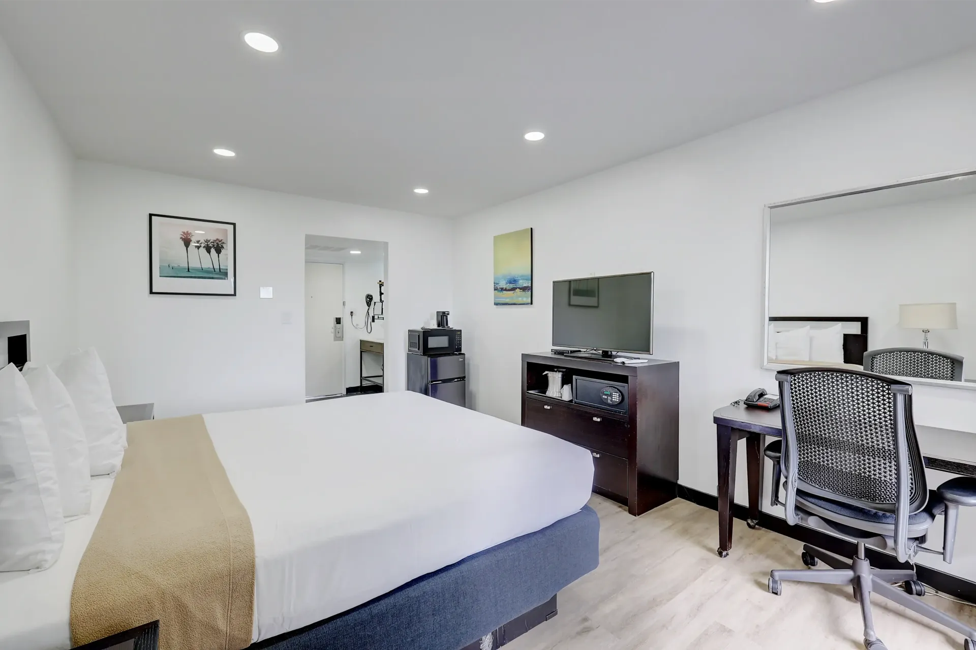 Bedroom with king bed, TV, desk, and small microwave. White walls, light wood floors.