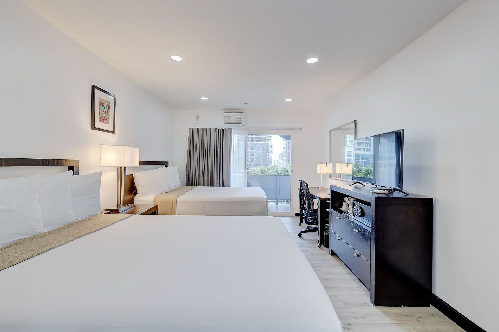 A hotel room with two queen beds, a desk, and a TV. White walls and bedding.