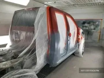 A truck body inside a paint booth, covered in plastic masking.