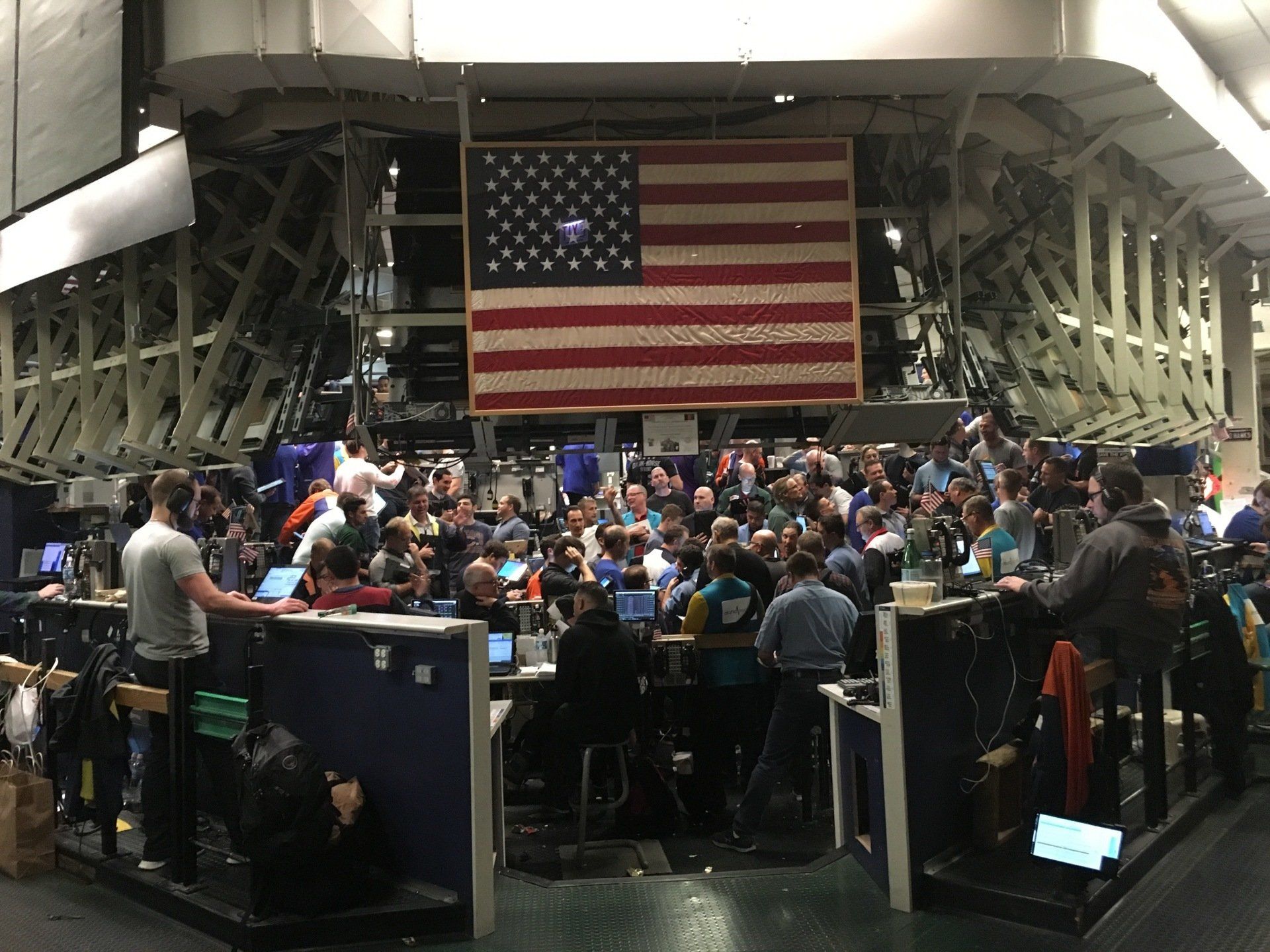 A large american flag hangs above a crowd of people