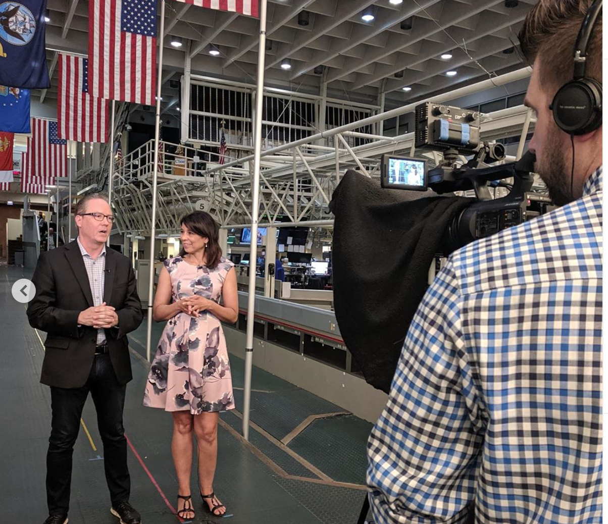 A man in a plaid shirt is recording a woman in a pink dress