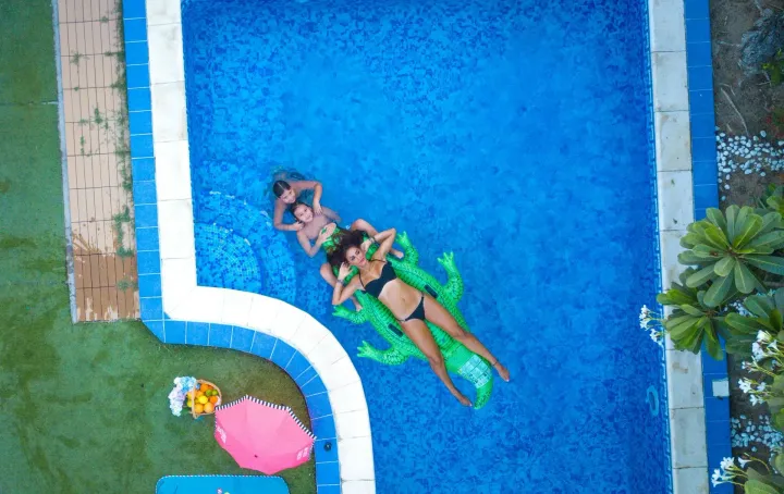 Aerial view of a family relaxing on a green alligator float in a blue pool.