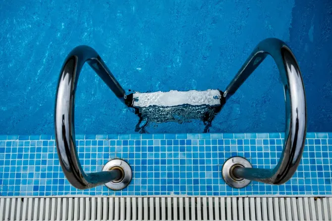 Symmetrical view of a pool ladder and steps in crystal clear blue water.