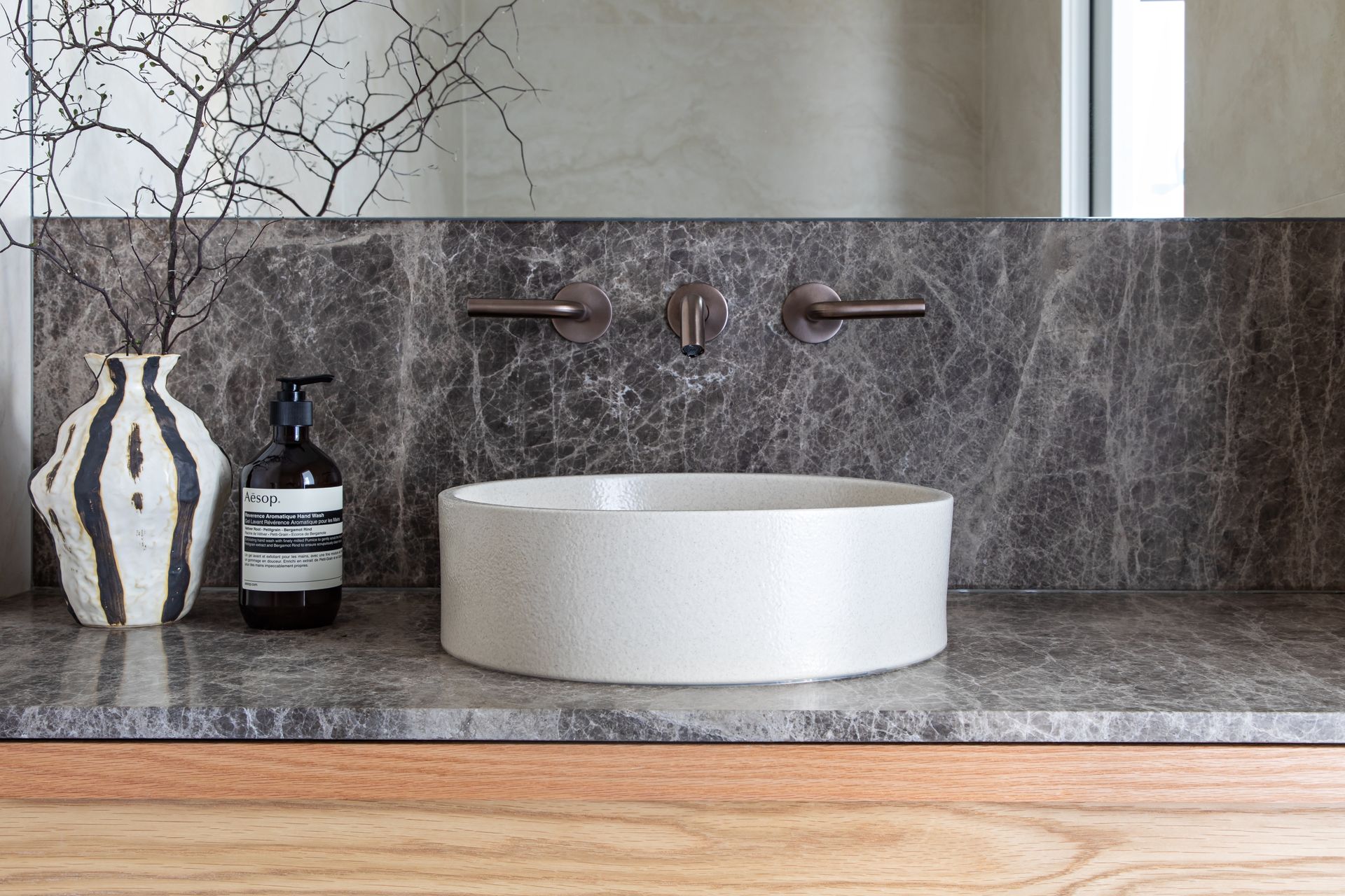 Modern bathroom vanity with a round white basin, marble splashback and wall-mounted bronze taps.