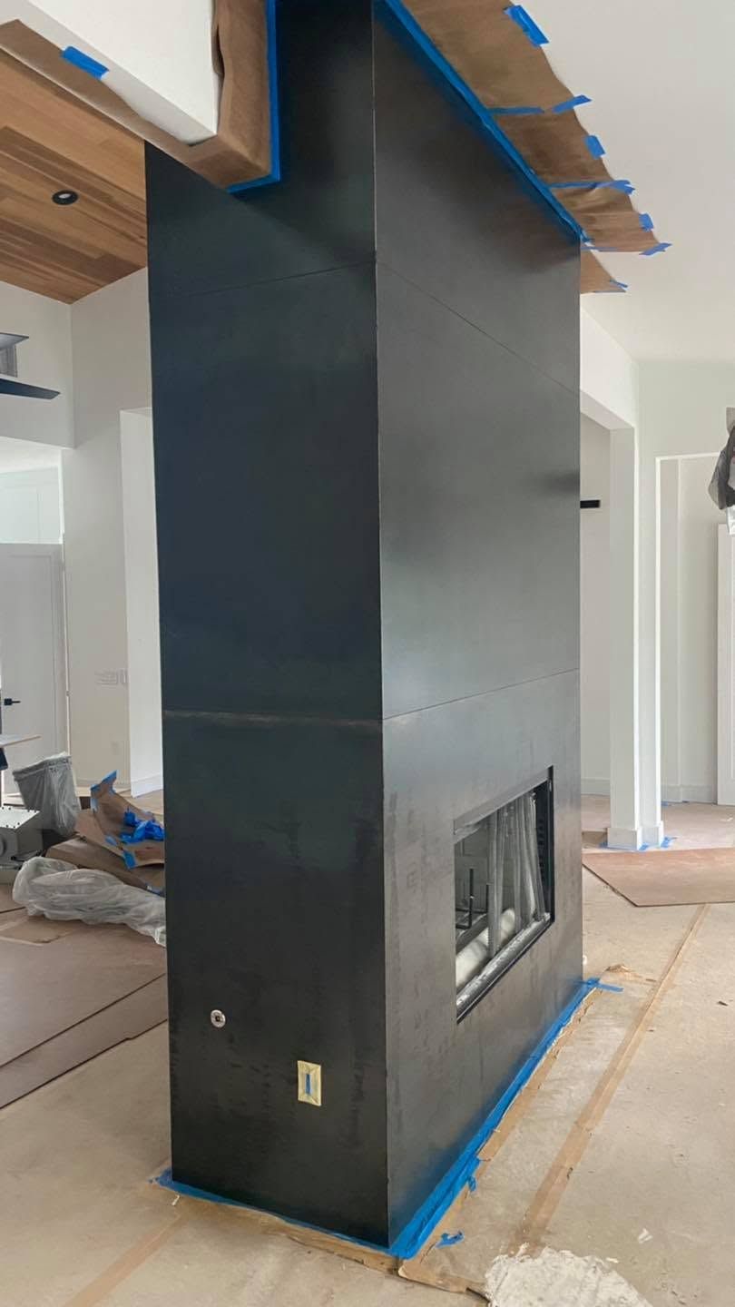 Black fireplace chase under construction in a home, taped with blue painter’s tape and centered on a living room wall