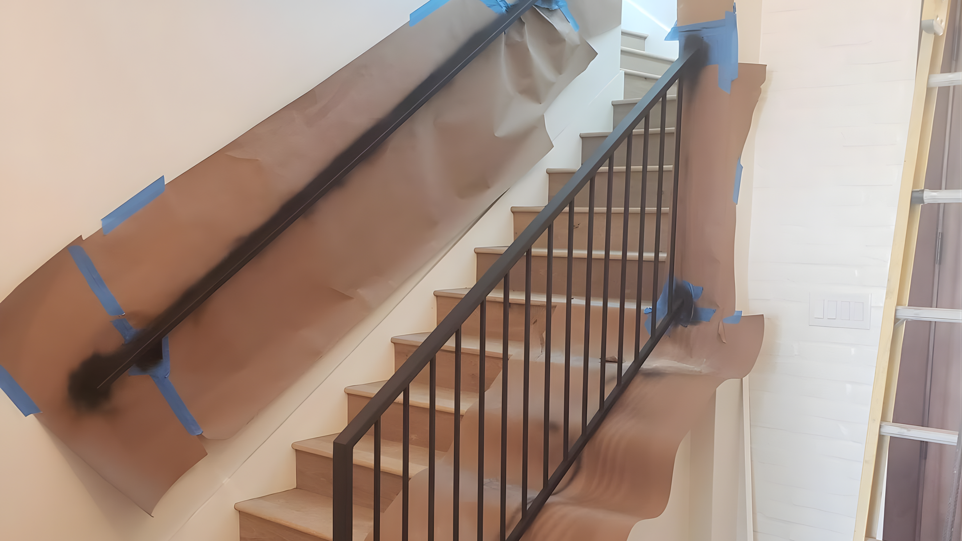 Stairwell with a black metal railing and protective cardboard covering the walls and handrail during renovation