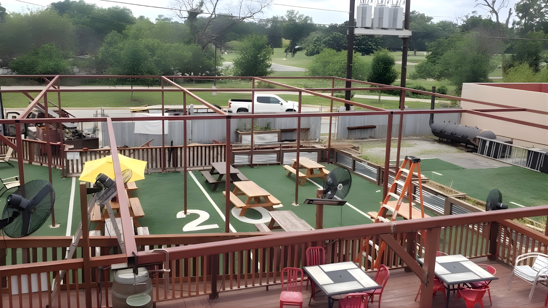 Outdoor mini-golf course with red railings, colorful obstacles, and a parking lot beyond