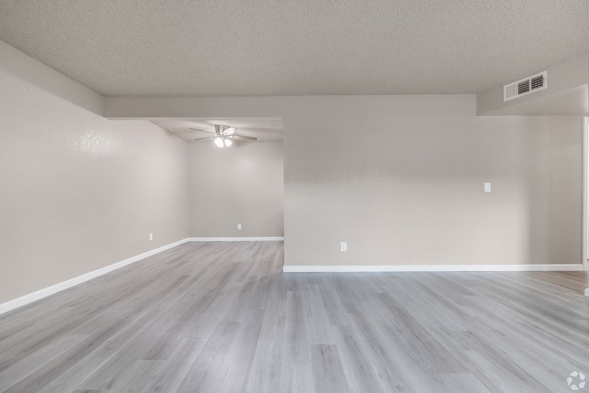 Empty living room with gray wood-look flooring, light gray walls, and a ceiling fan.