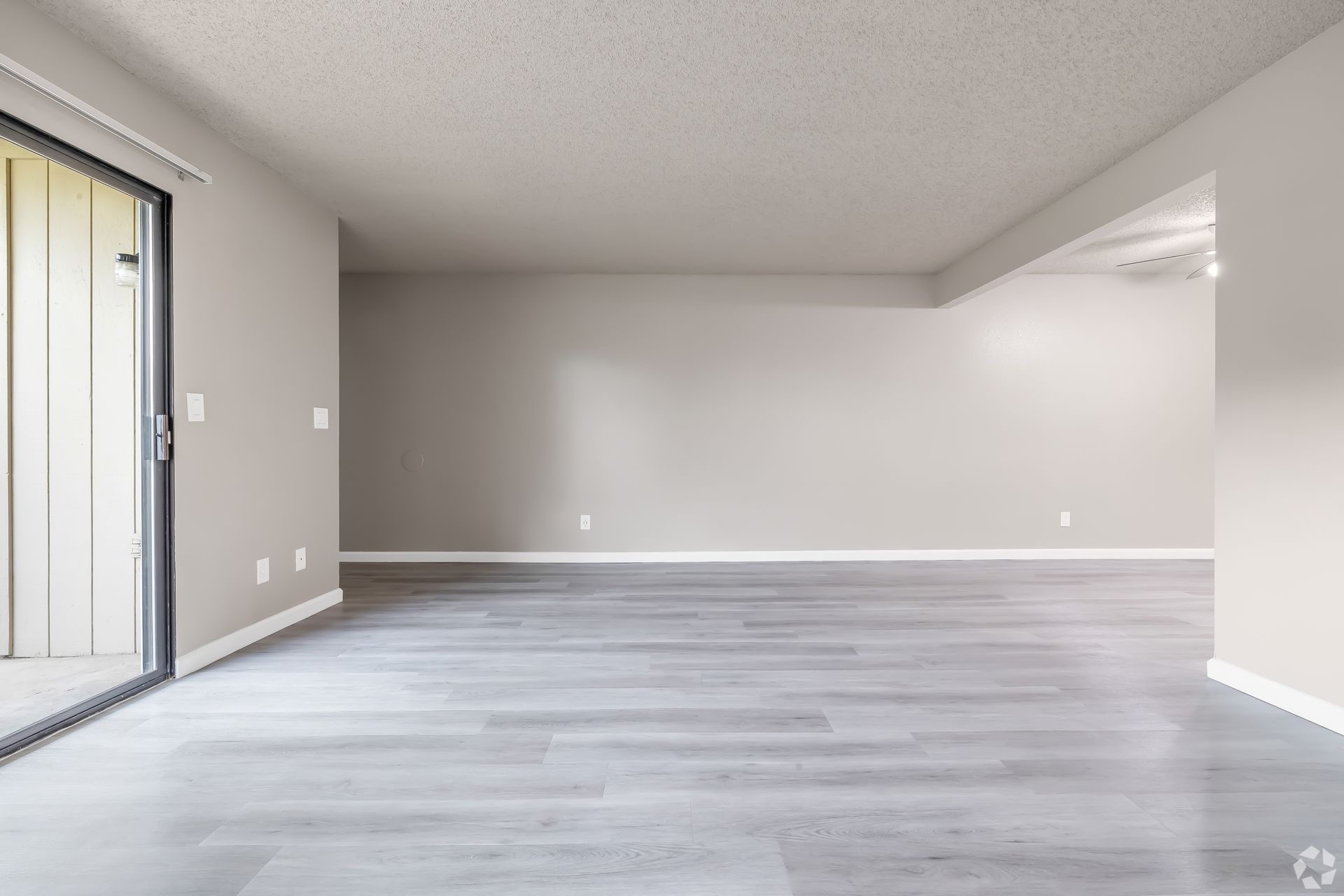 Empty, bright living room with gray floors, walls, and a sliding door to the outside.