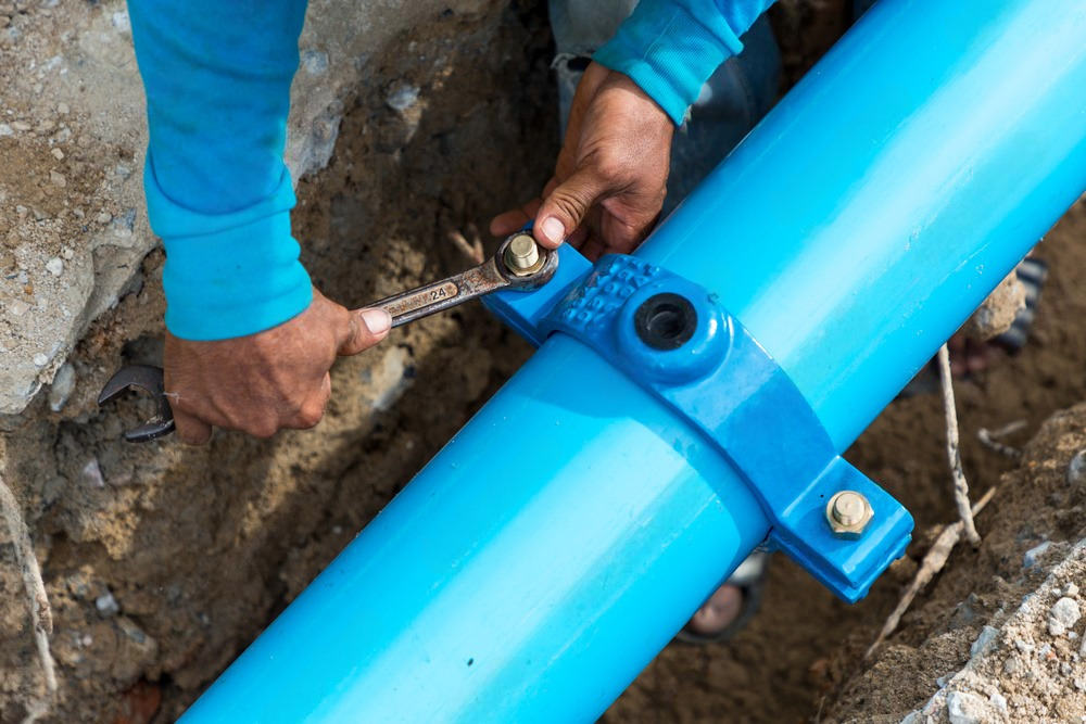 A man is working on a blue pipe in the dirt.