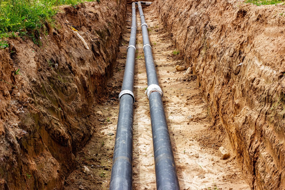 Two pipes are being installed in a trench in the dirt.