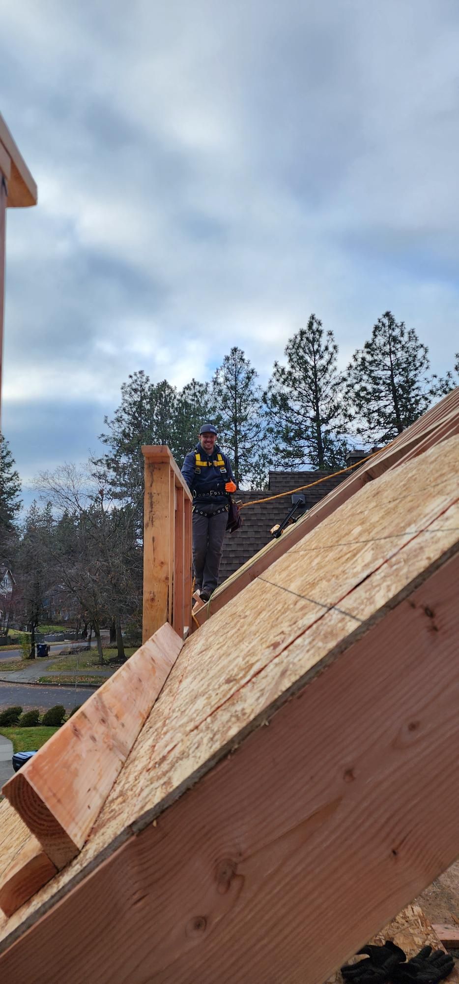 Person standing on a wooden roof frame outdoors under a cloudy sky