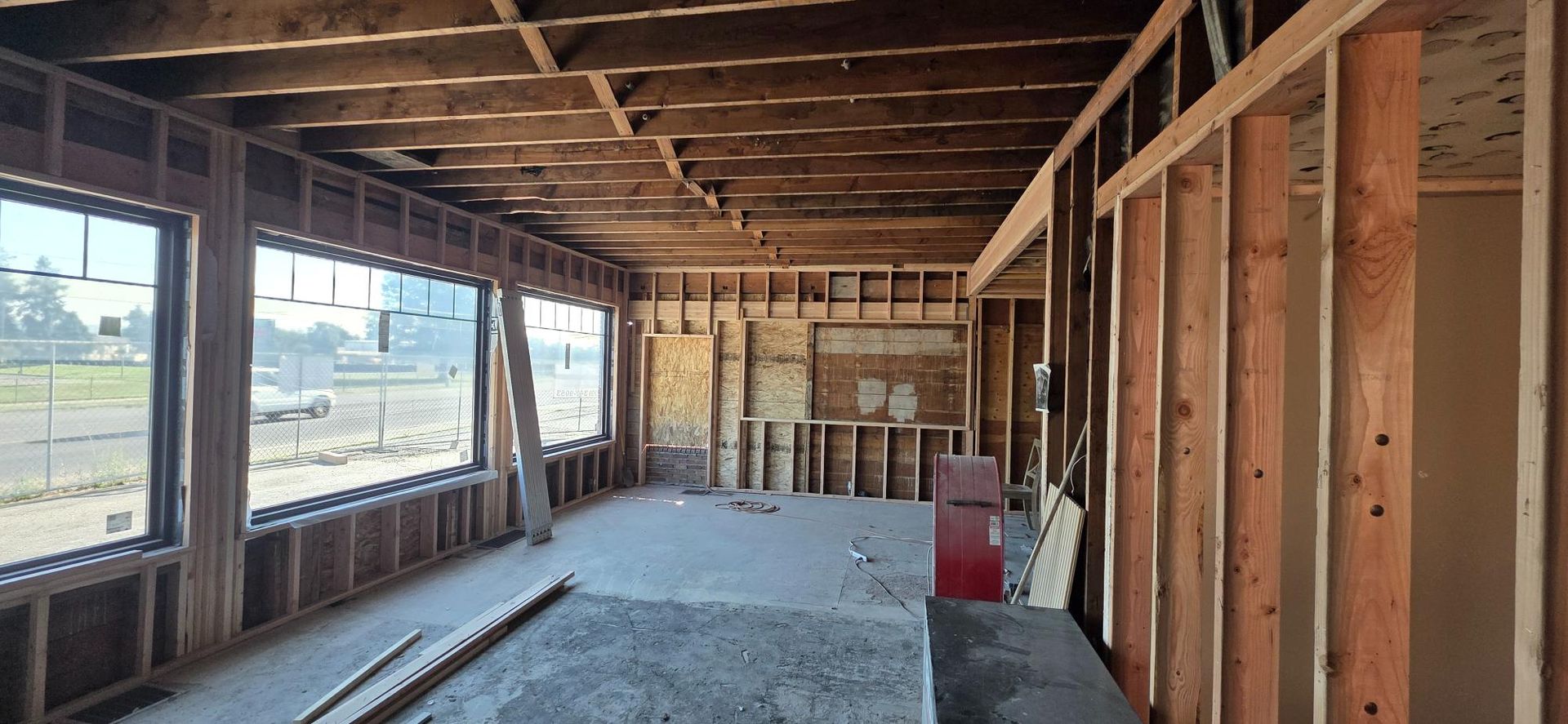 Interior of a house under construction with exposed wood framing, long windows, and concrete floor