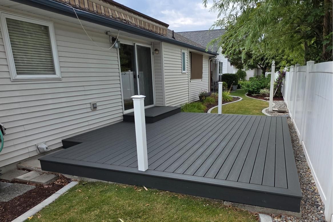 Backyard deck with gray boards, white support posts, and a white fence beside a house