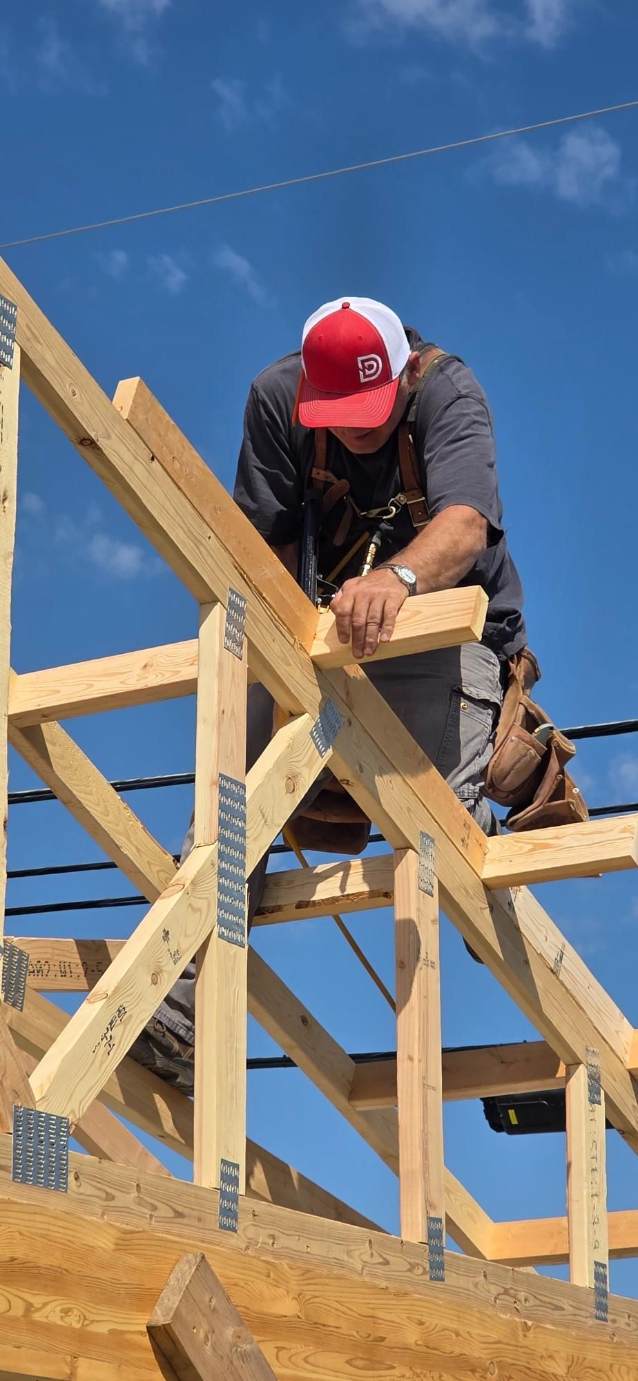 Construction worker in red cap assembling a wooden roof frame under a blue sky