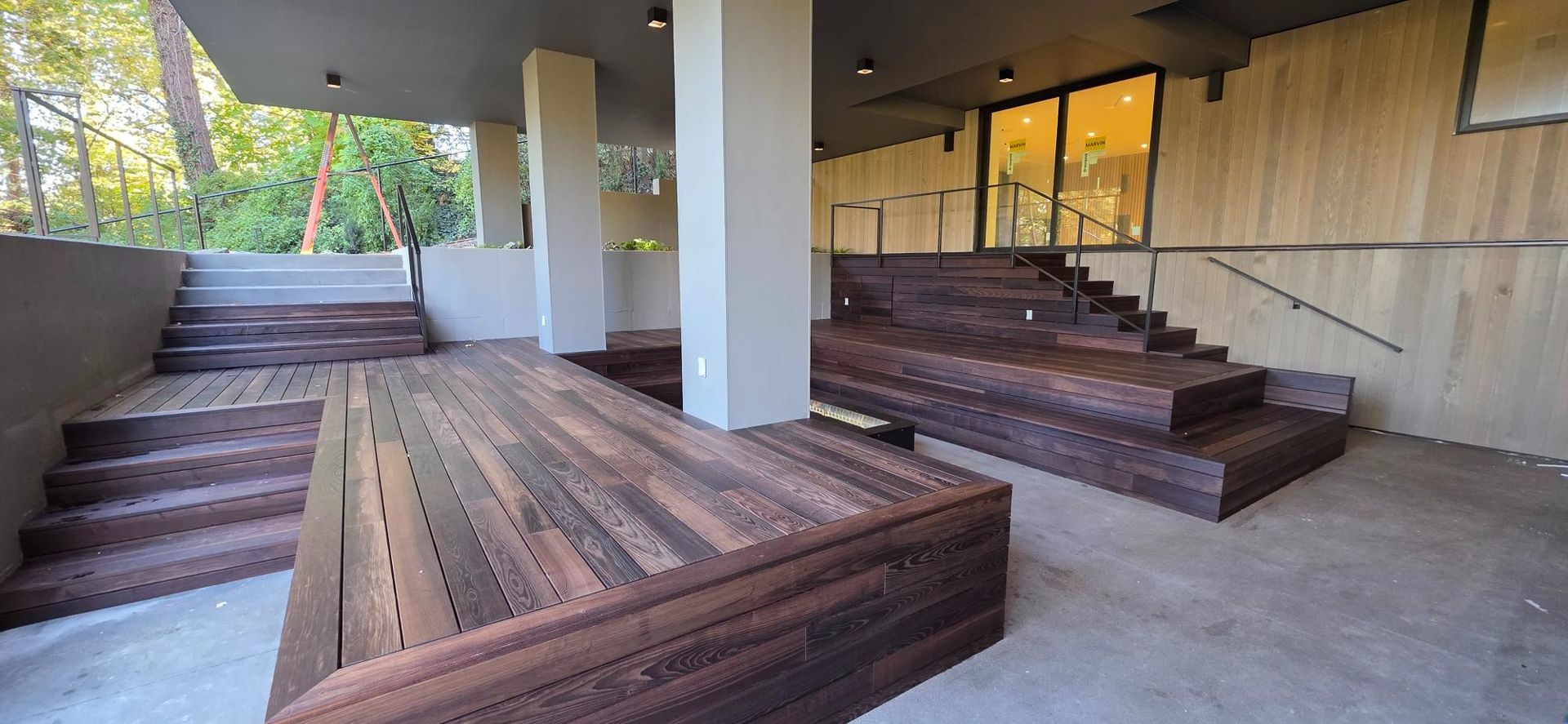 Outdoor concrete seating area with wooden benches, stairs, and a covered walkway.