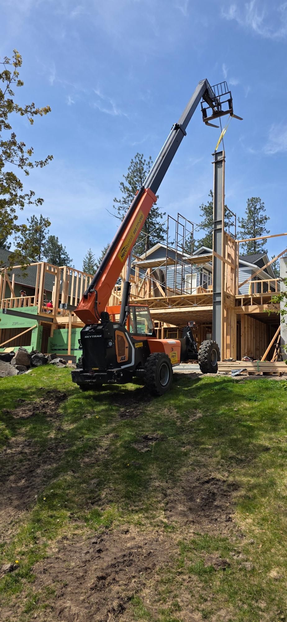 Construction crane lifting materials beside a wooden house under construction in a wooded yard