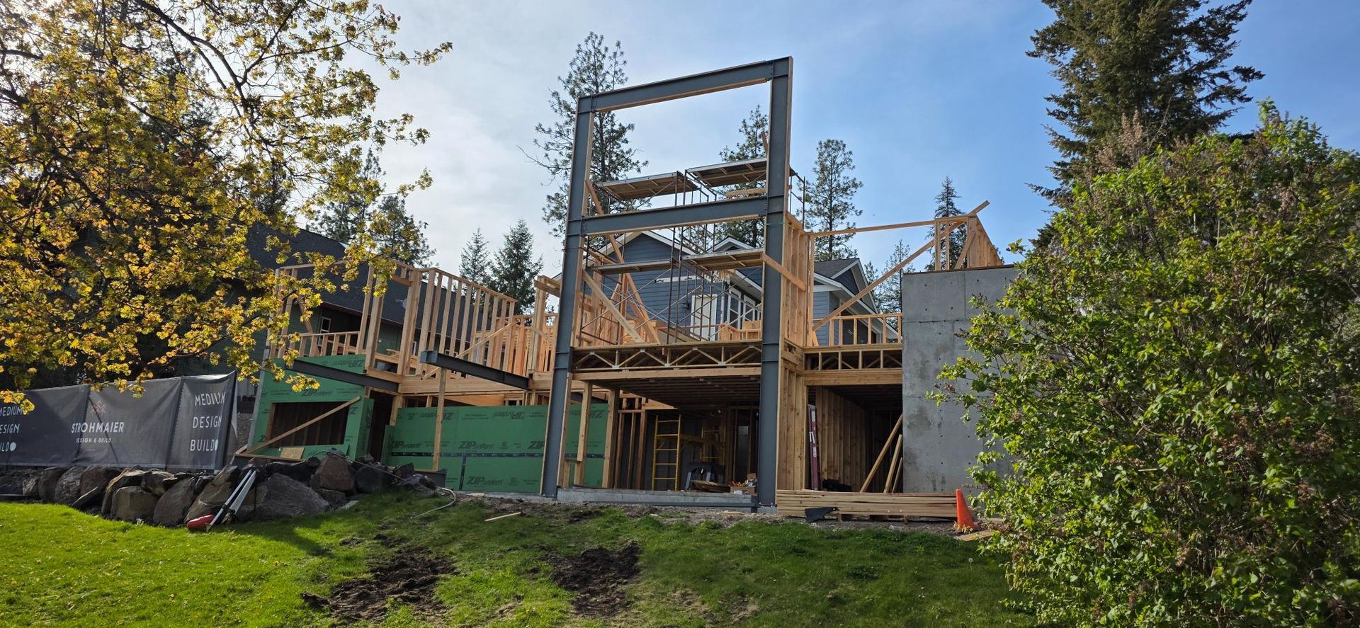 Partially built wooden house with scaffolding and a tall steel frame in a grassy yard