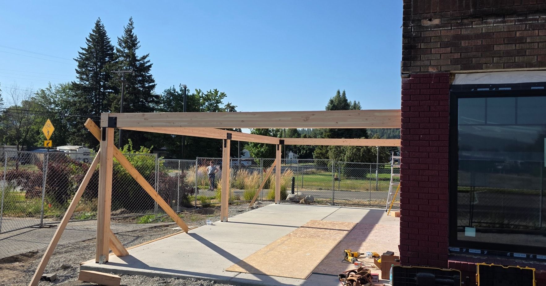 Outdoor construction site with wooden beams and supports beside a brick building under a blue sky