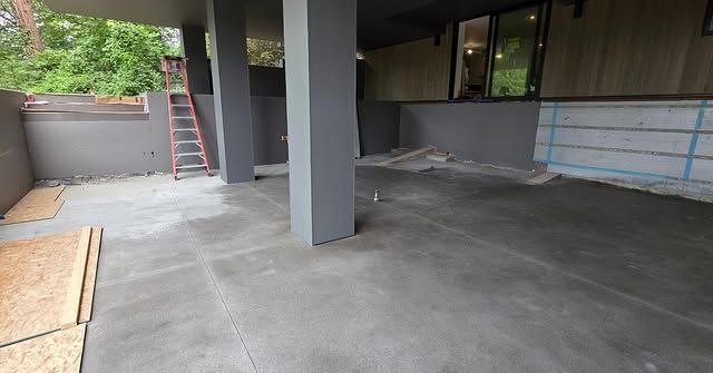 Empty concrete patio under a house with support pillars and a partially covered wall